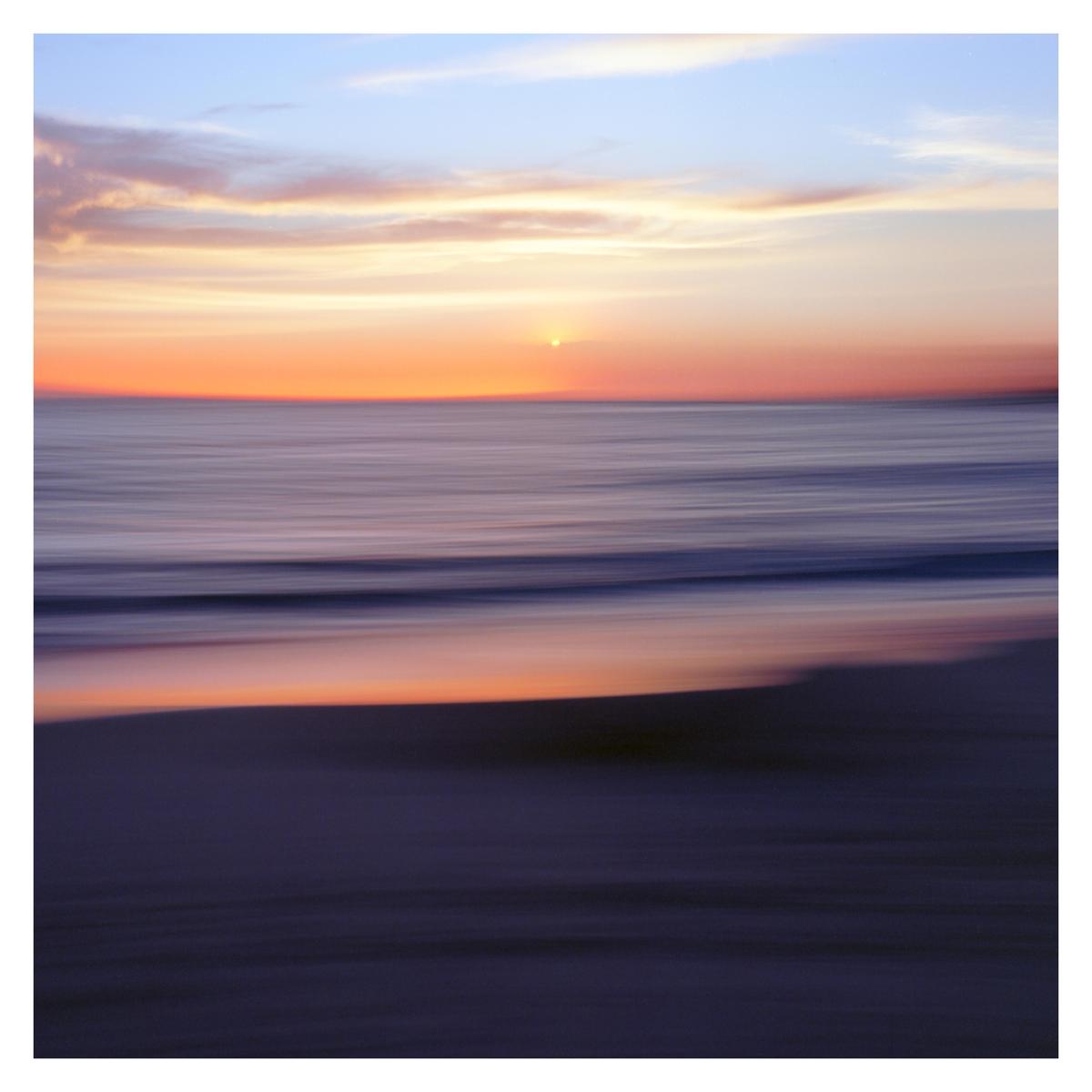The sun sets over the ocean and beach, with motion blur.