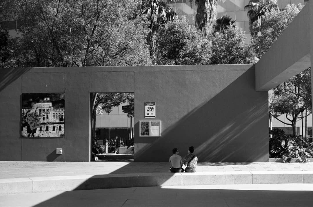 Two people sit on a ledge in front of a wall with a "Free Wi-Fi" sign and a poster of a building.