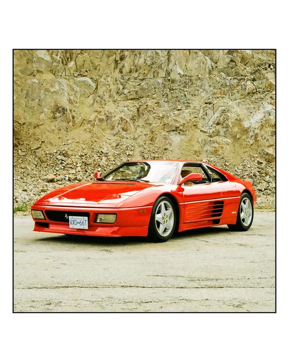 A red sports car is parked on an asphalt surface in front of a rocky cliff.