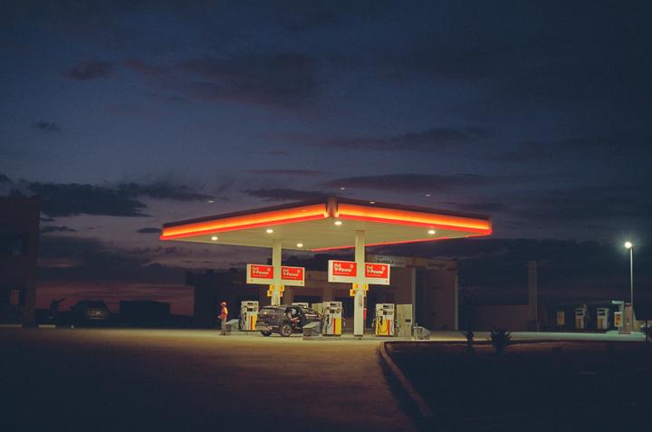 A gas station with a car and a man standing next to a pump is illuminated at dusk.