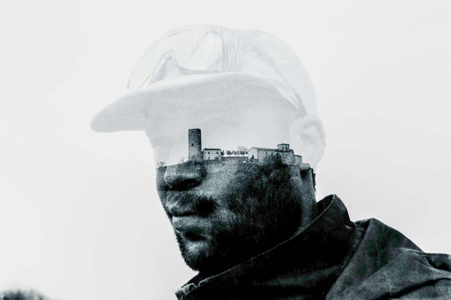 A double exposure shows a man wearing a cap with a village and tower superimposed on his head.