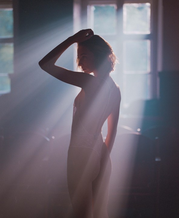 A woman stands in a room with light rays shining through a window.