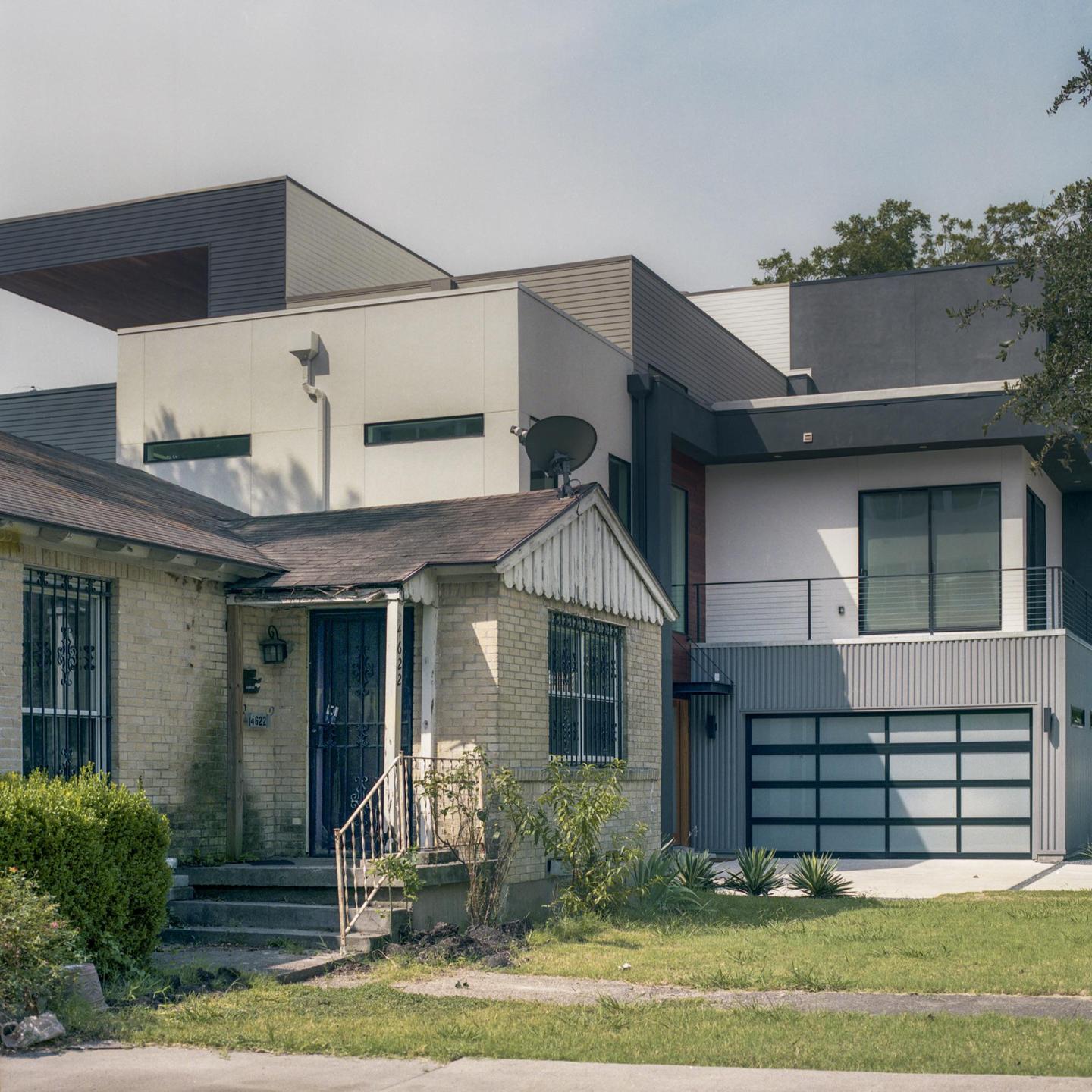 An old brick house with a porch and security bars stands next to a modern house with a garage and balcony.
