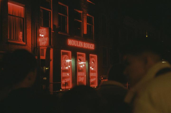 A building with red neon signs for "Moulin Rouge" is visible at night, with blurred people in the foreground.