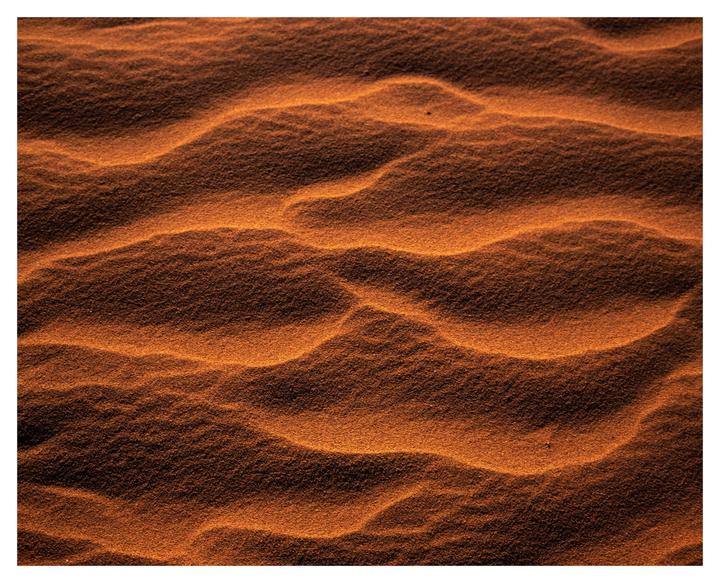 The image shows a close-up of sand dunes with ripples and shadows.