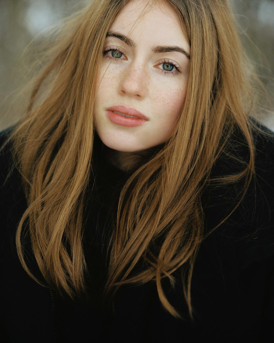 A woman with long hair and freckles looks directly at the viewer.