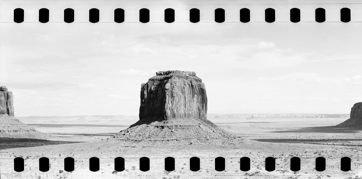 A large rock formation stands in a desert landscape under a cloudy sky.