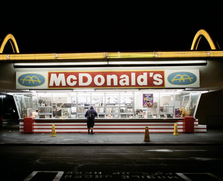 A person stands in front of a McDonald's restaurant at night.