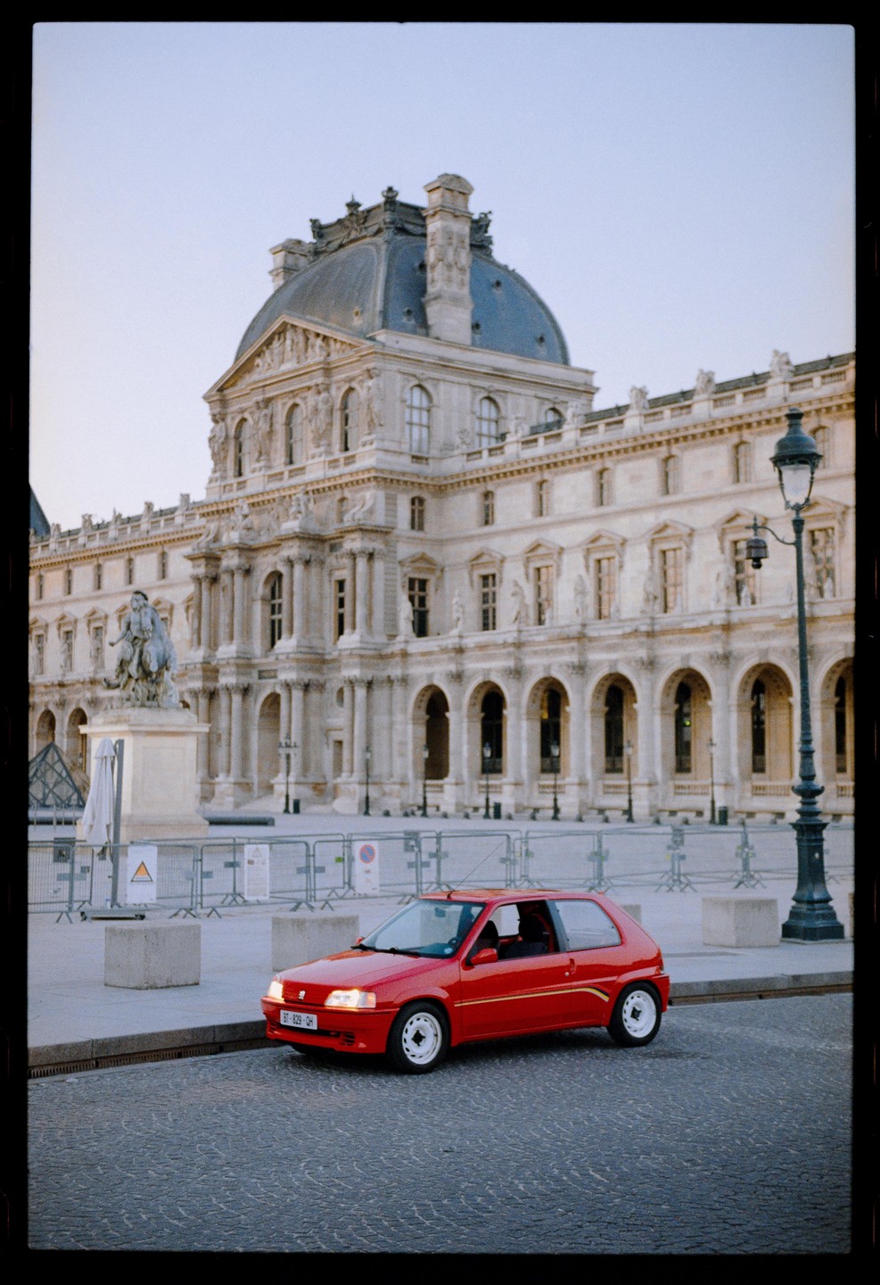 A red car is parked on a cobblestone street in front of a large, ornate building with a domed roof.