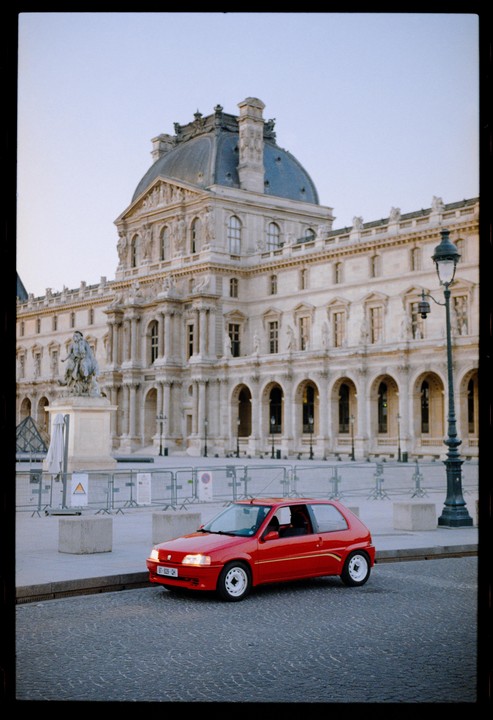 A red car is parked on a cobblestone street in front of a large, ornate building with a domed roof.