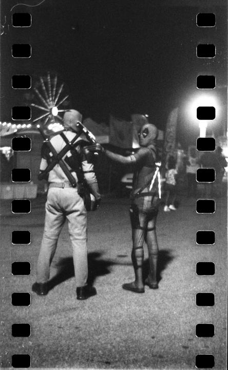 Two people in costume stand on a street at night with a Ferris wheel in the background.
