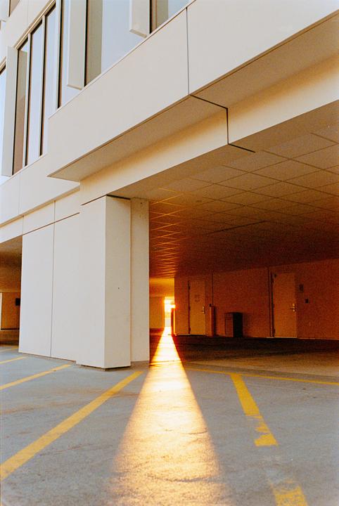 Sunlight streams through a keyhole-shaped opening in a parking garage, illuminating the floor with a bright, warm glow.