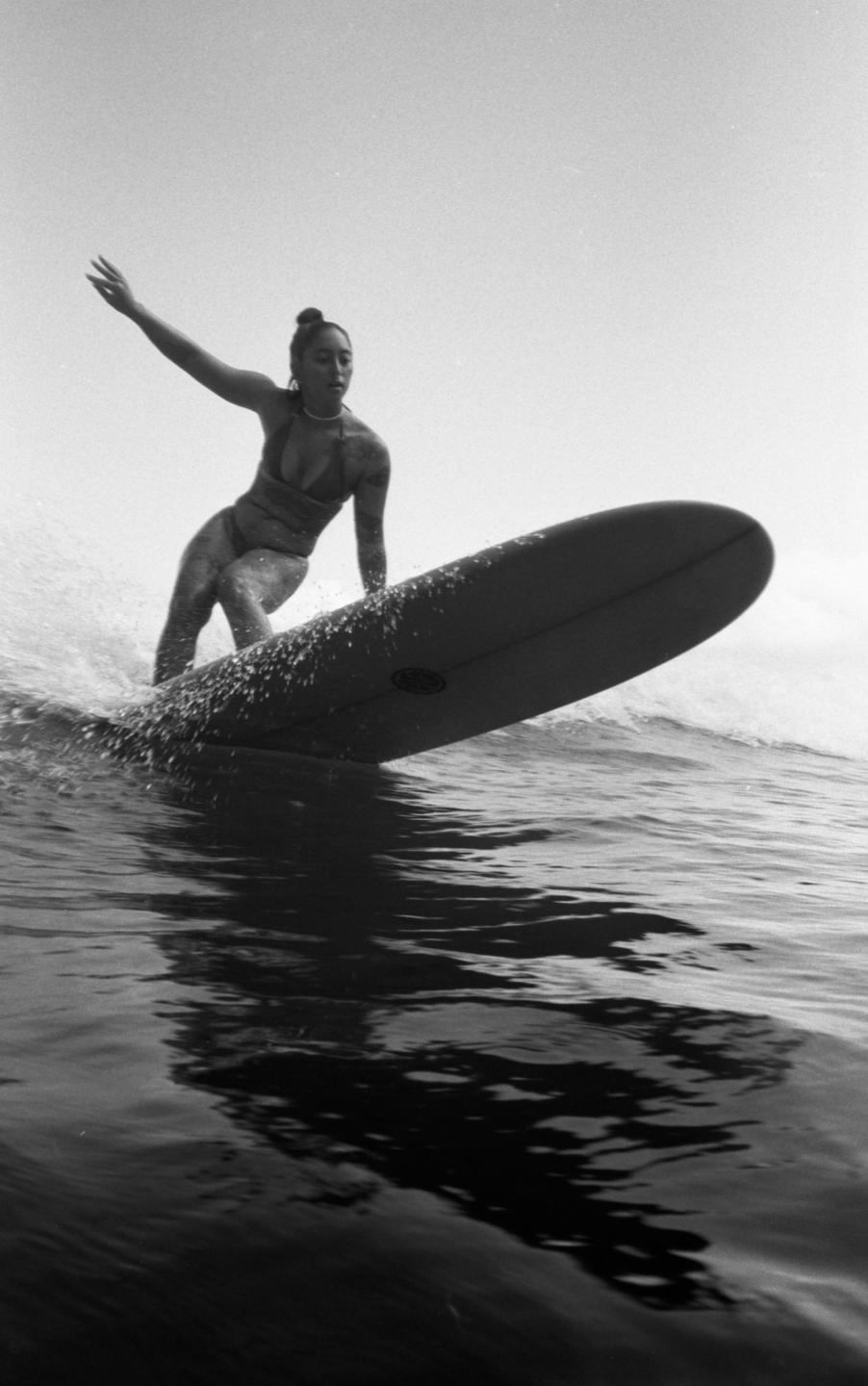 A woman in a bikini surfs on a longboard, with water splashing around the board.