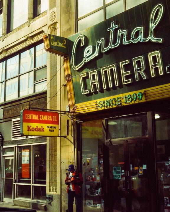 A man stands outside Central Camera Co. with a neon sign above the entrance.