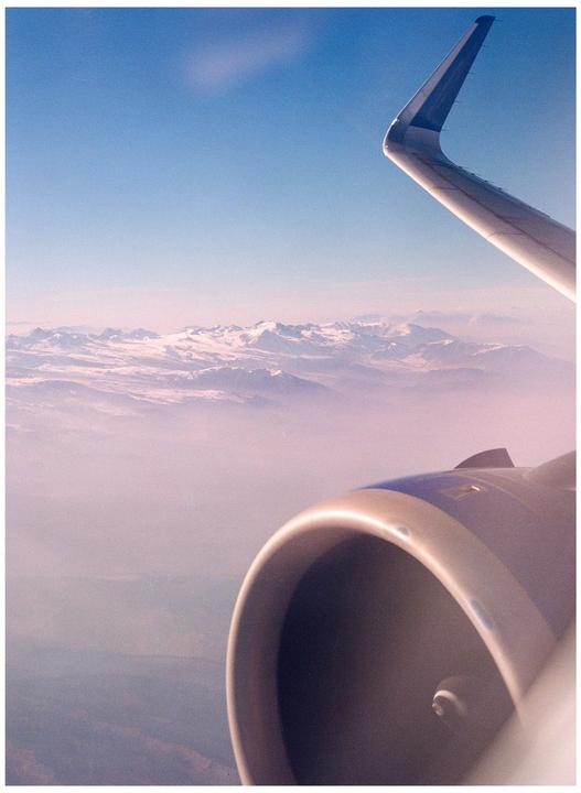 An airplane wing and engine are visible above a hazy mountain range.