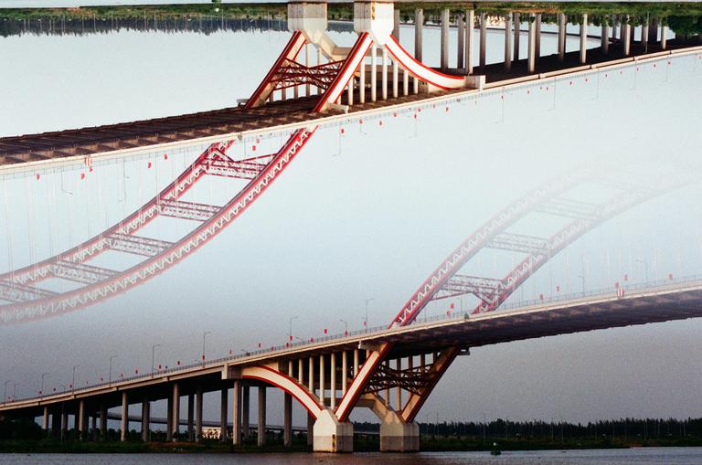 A double exposure shows a red and white bridge over water, with one exposure inverted.