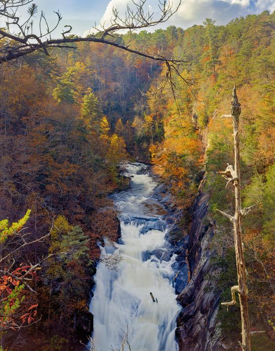A river flows through a gorge with a waterfall and autumn foliage.
