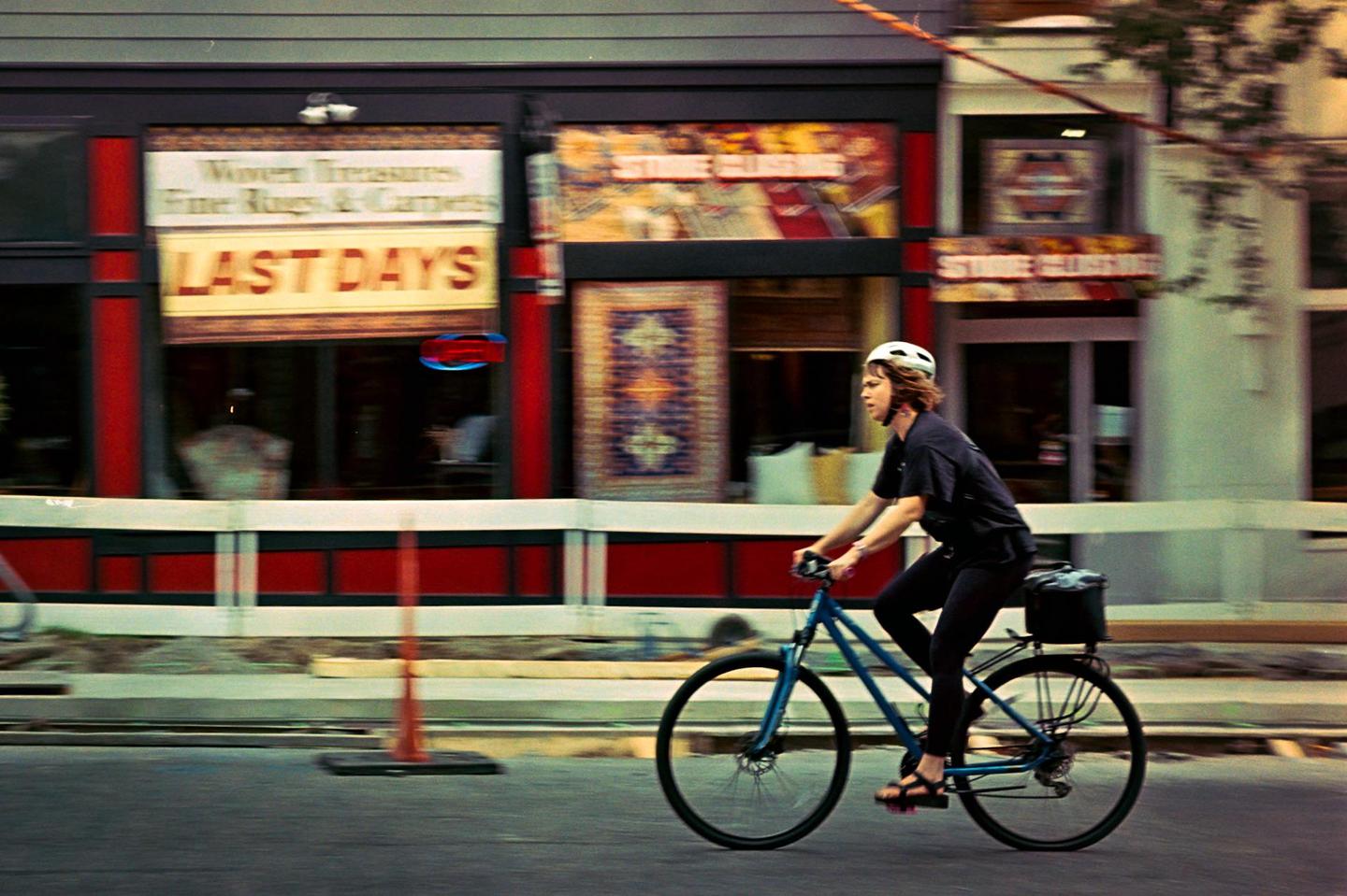 A woman rides a bicycle past a storefront with a "LAST DAYS" sign.