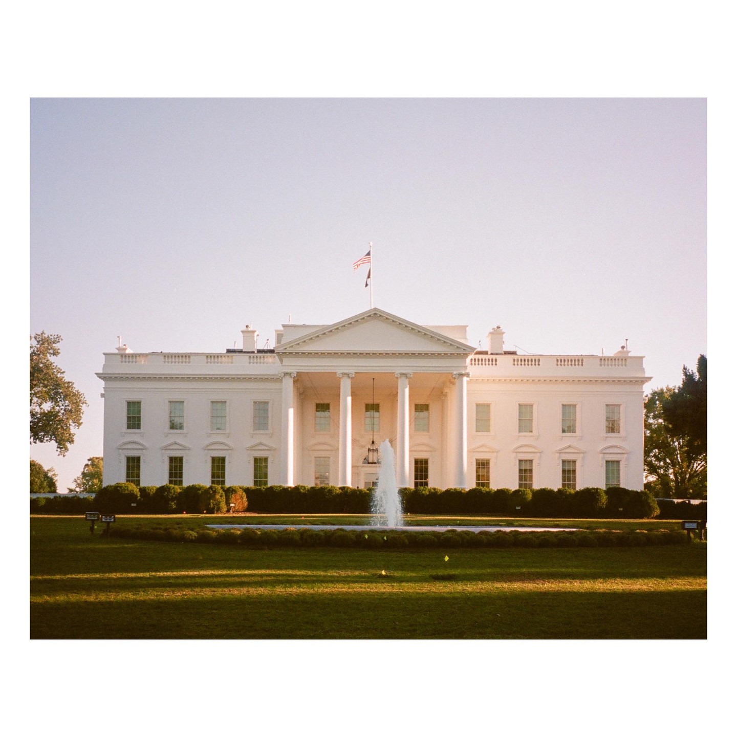 The White House is visible behind a fountain and a green lawn.