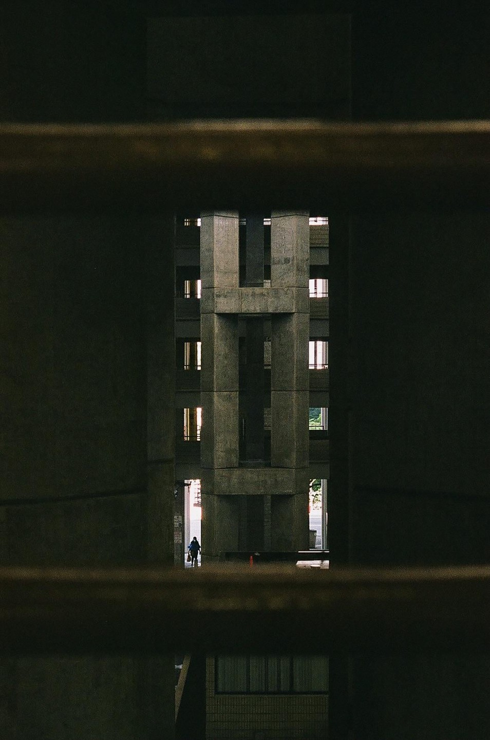 A person walks through a brutalist concrete building with many windows, framed by dark horizontal bars.