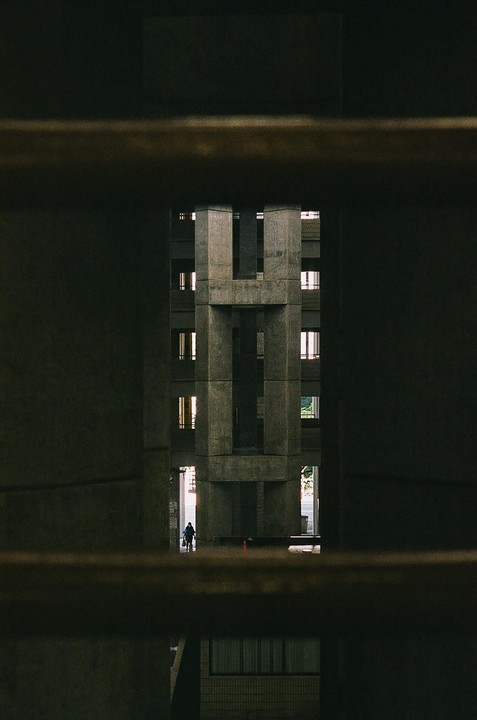 A person walks through a brutalist concrete building with many windows, framed by dark horizontal bars.
