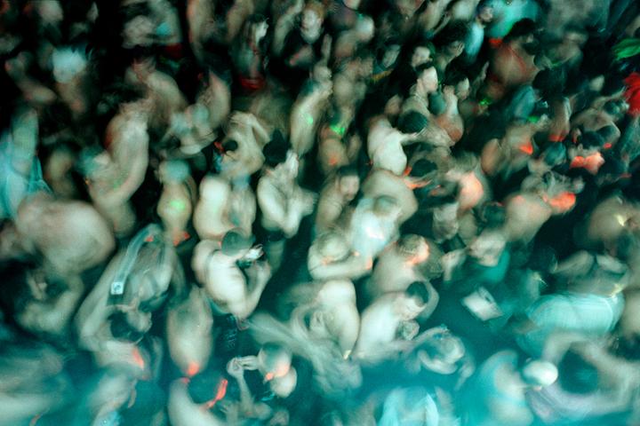 A blurry overhead shot captures a crowd of people dancing in a dark, neon-lit space.
