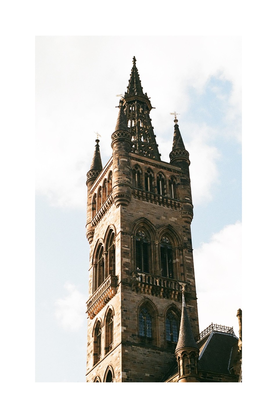 A tall, ornate stone tower with multiple spires and arched windows stands against a bright sky with a few clouds.
