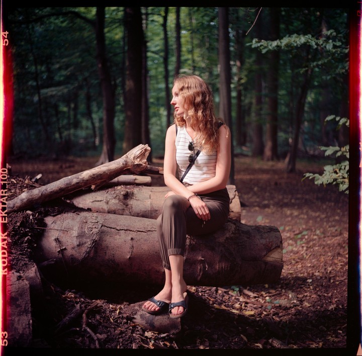 A woman with long, curly hair sits on a fallen tree trunk in a forest.