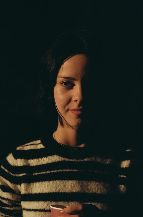 A woman in a striped sweater holds a cup, with half her face illuminated by light.