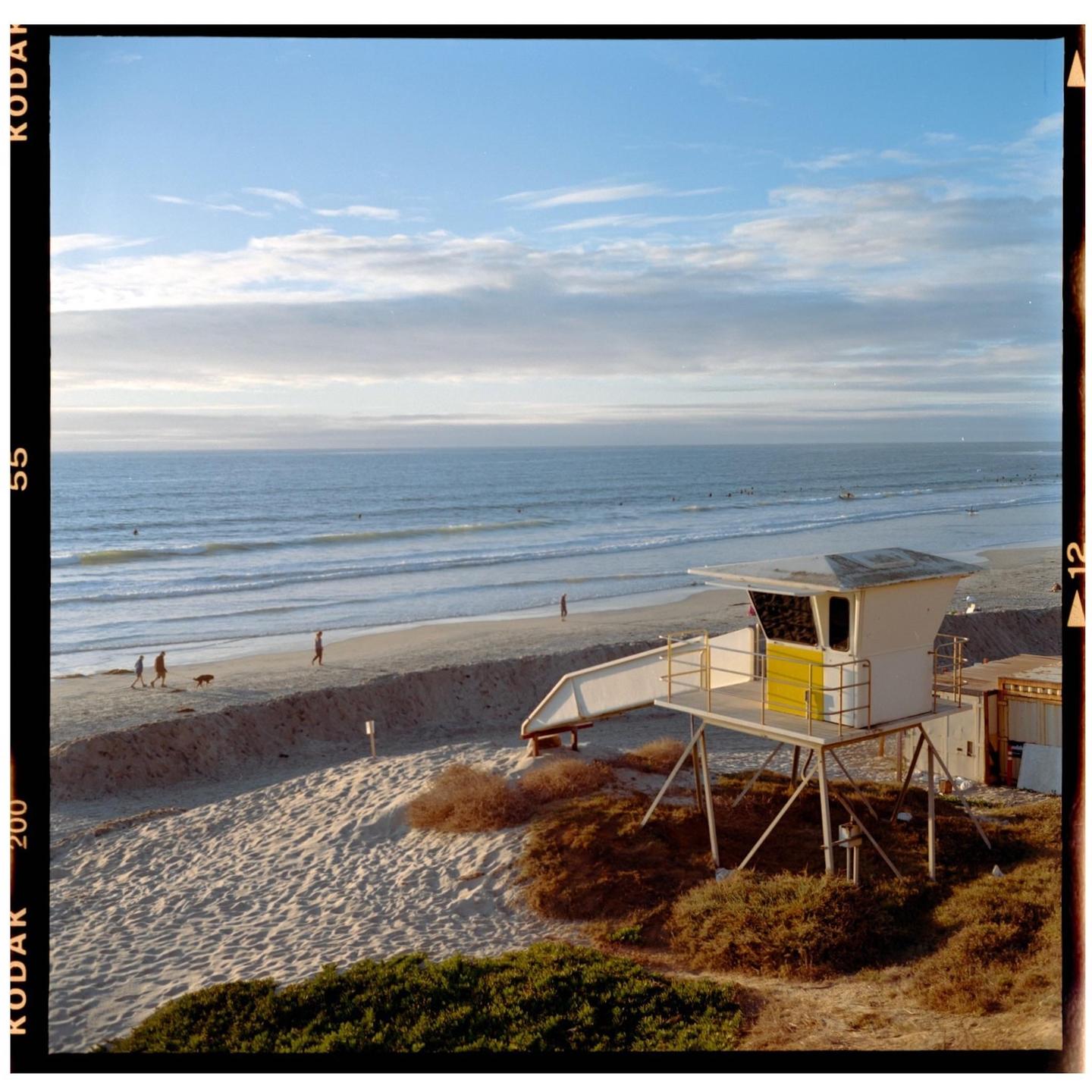 A lifeguard tower stands on a sandy beach next to the ocean under a partly cloudy sky.