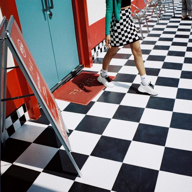 A person walks on a black and white checkered floor past a red welcome mat and a blue door.