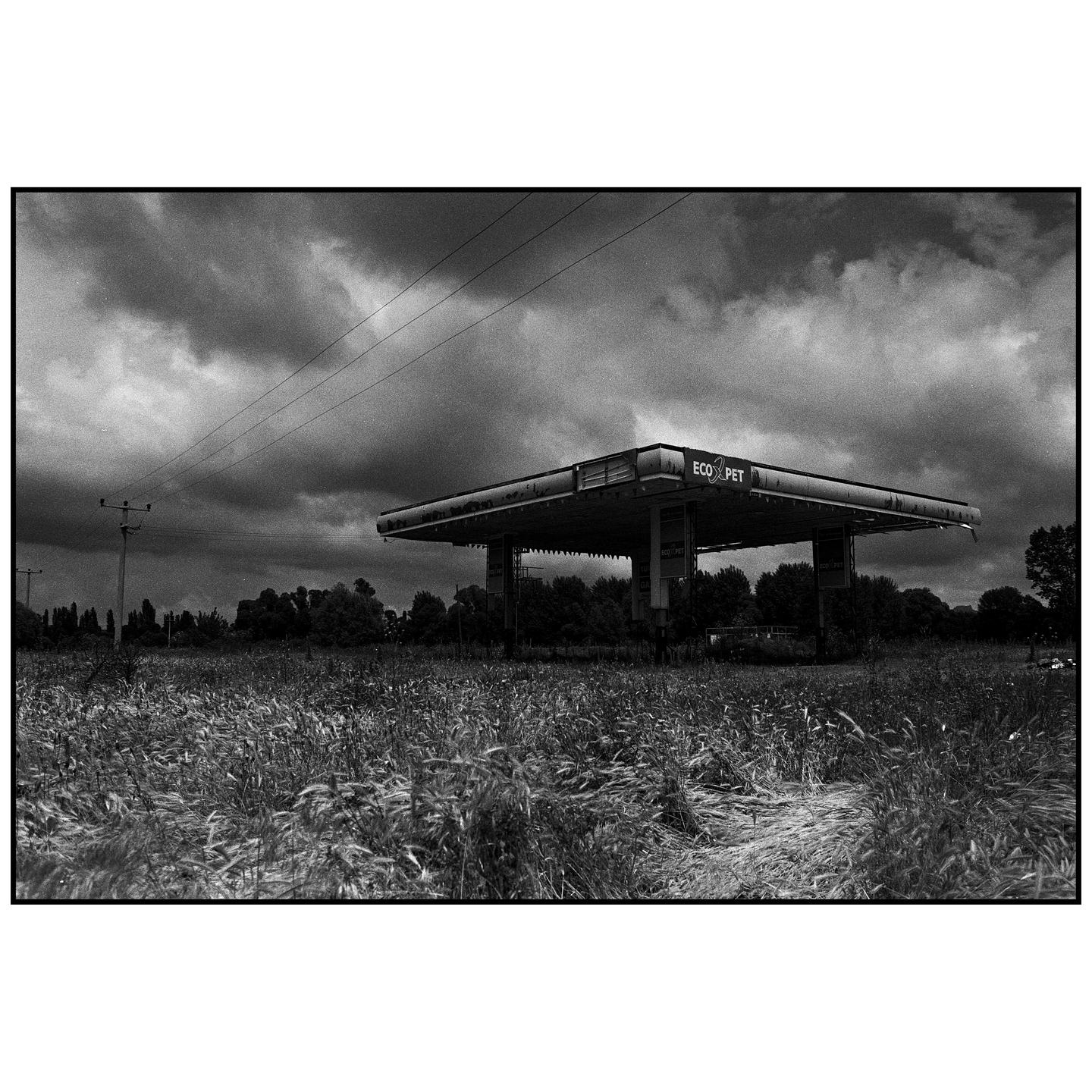An abandoned gas station stands in a field under a cloudy sky.
