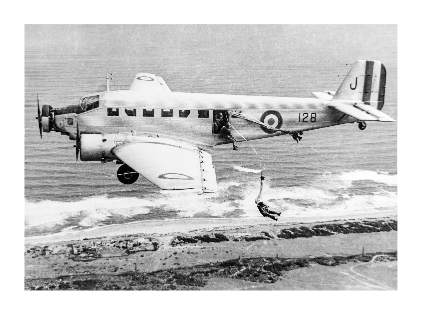 A paratrooper descends from an airplane over a coastline with waves crashing on the shore.
