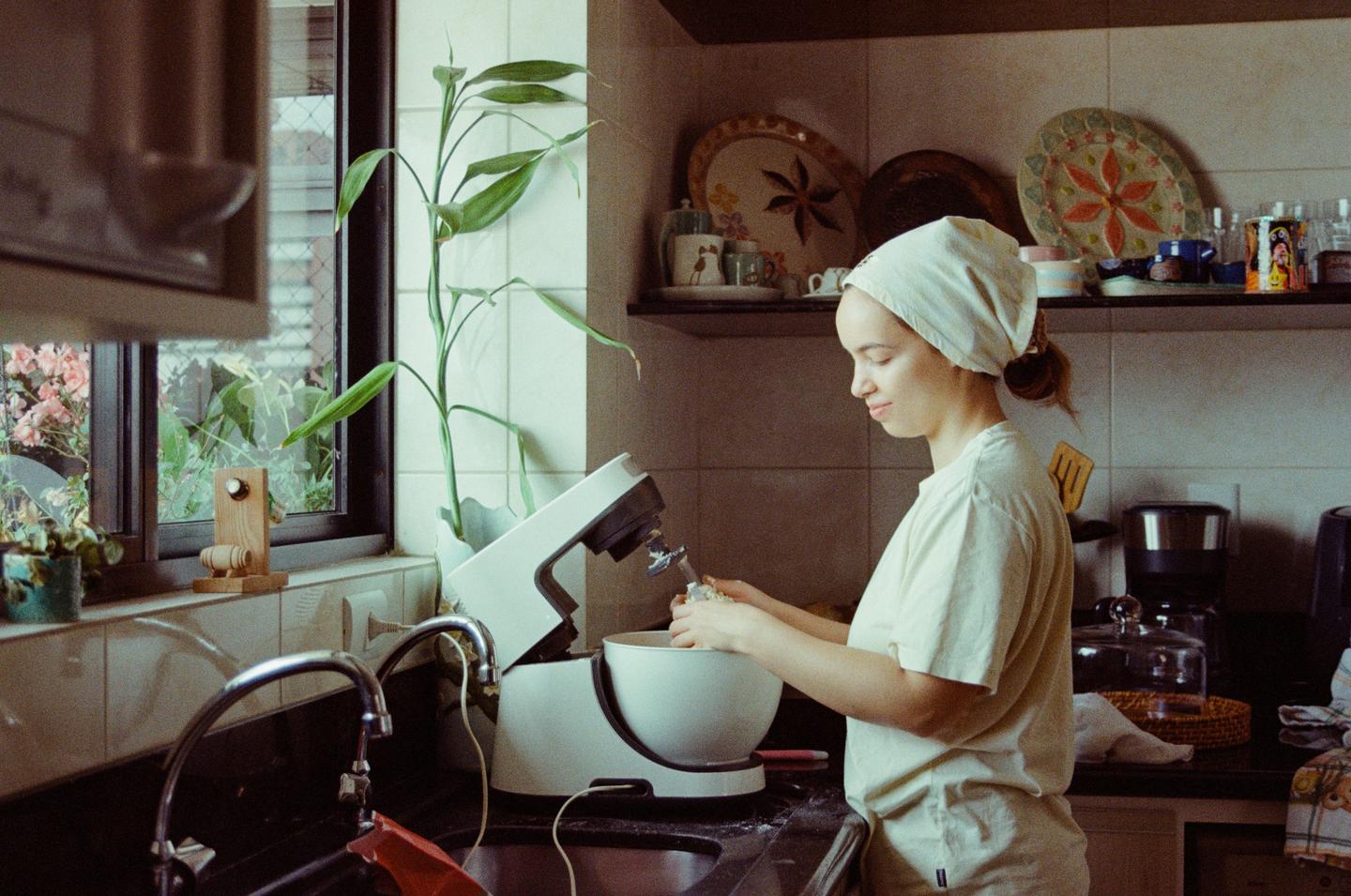 A woman wearing a headscarf is preparing food with a stand mixer in a kitchen.