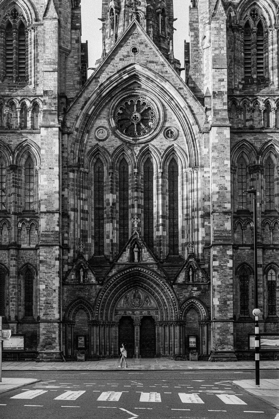 A woman walks across a crosswalk in front of a large, ornate cathedral.