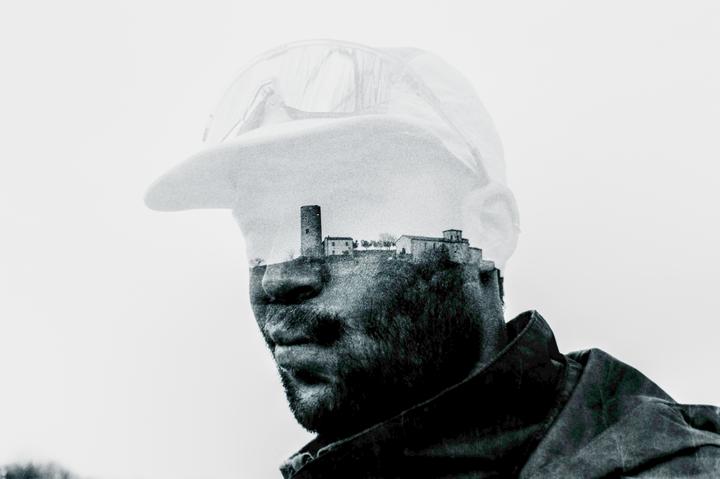 A double exposure shows a man wearing a cap with a village and tower superimposed on his head.
