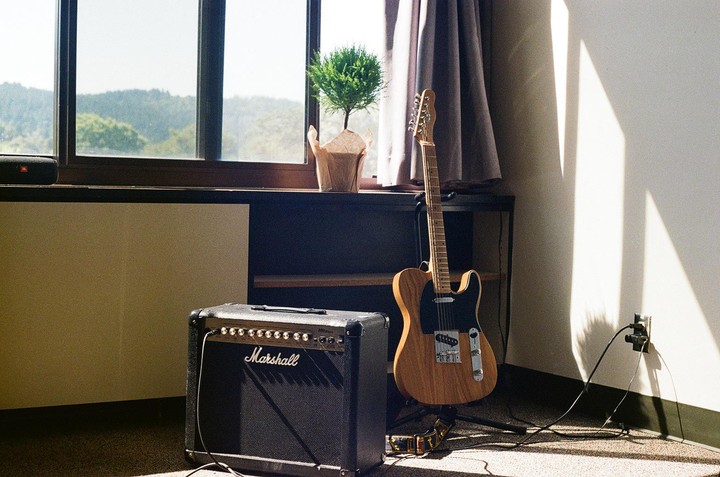 A guitar and amplifier sit in a sunlit room with a window looking out onto hills.