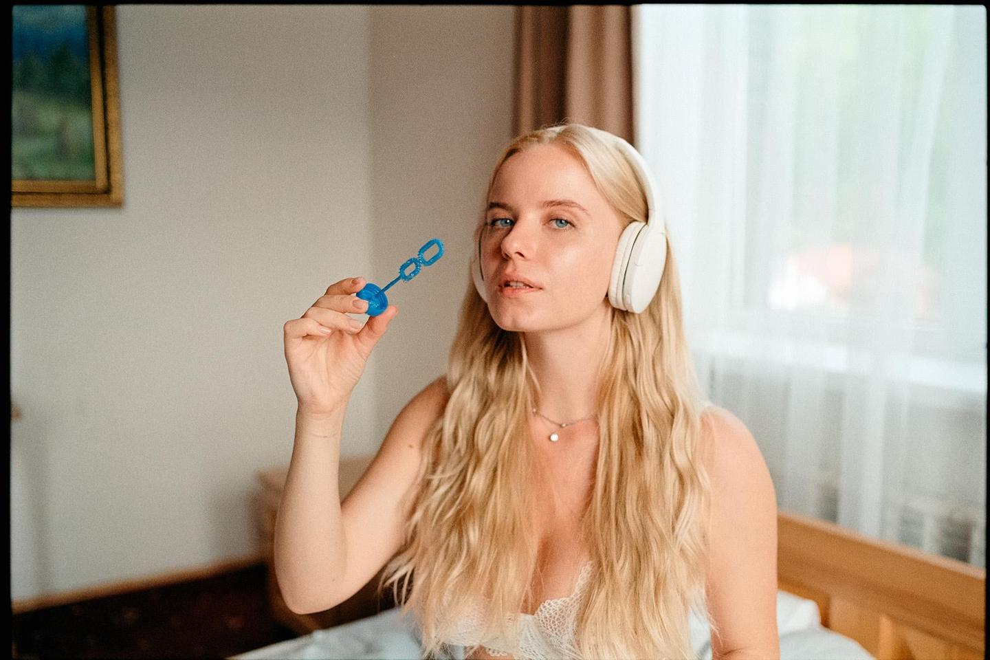 A woman with long blonde hair and headphones holds a bubble wand.