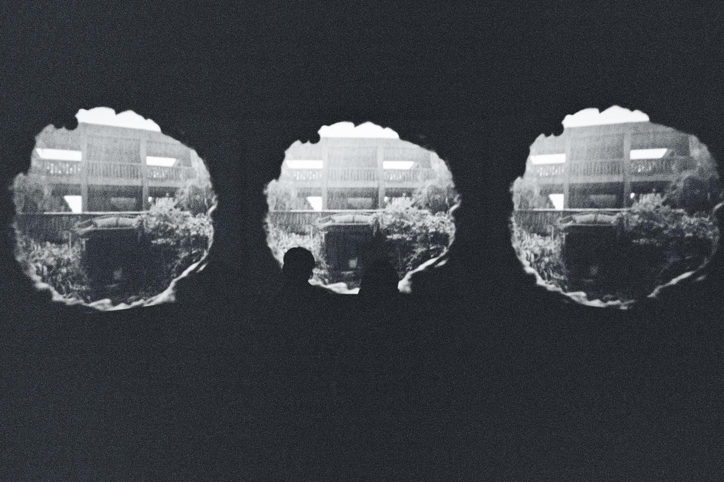 Three circular windows look out onto a building with balconies and lush foliage.