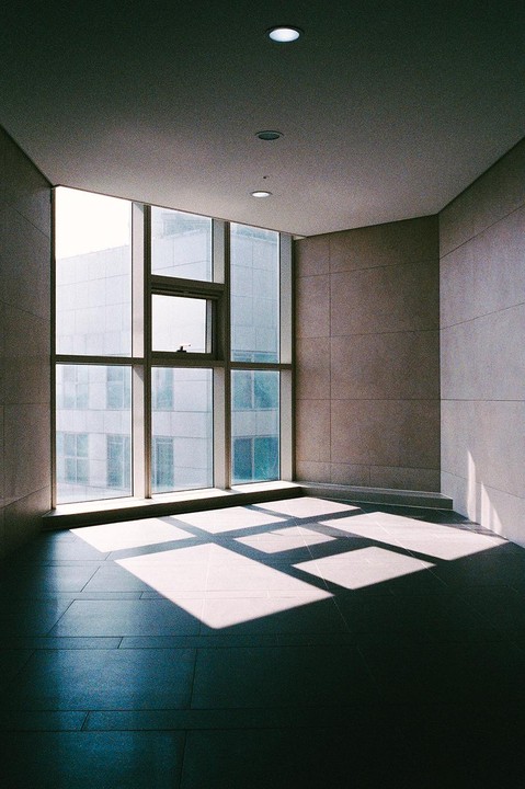 Sunlight streams through a large window, casting geometric shadows on the tiled floor of an empty room.