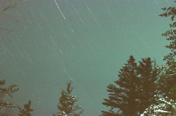 Star trails are visible in the night sky above snow-covered trees.