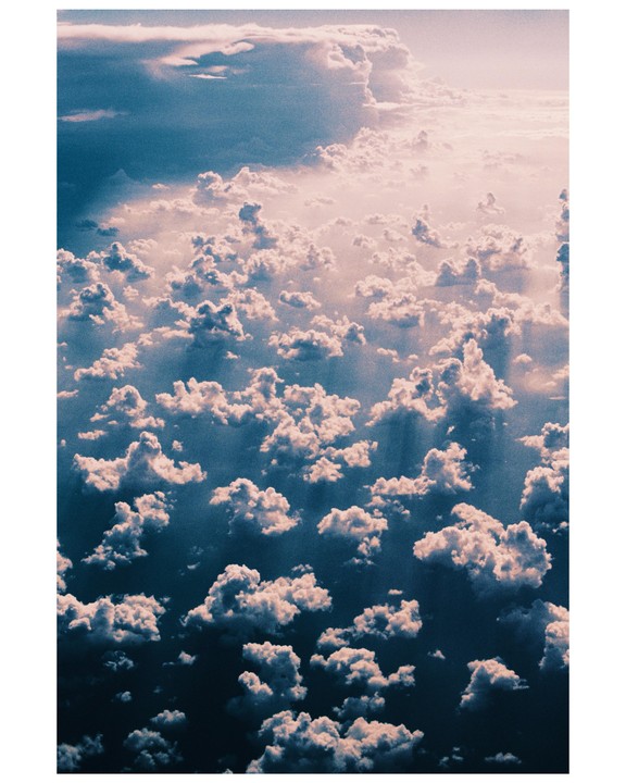 An aerial view shows a sky full of fluffy clouds with light rays shining through them.