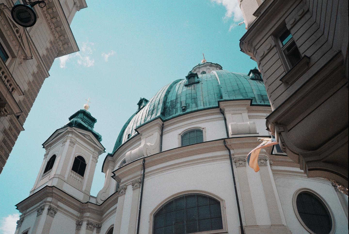 A low-angle view shows a white church with a green dome and steeple against a bright blue sky.
