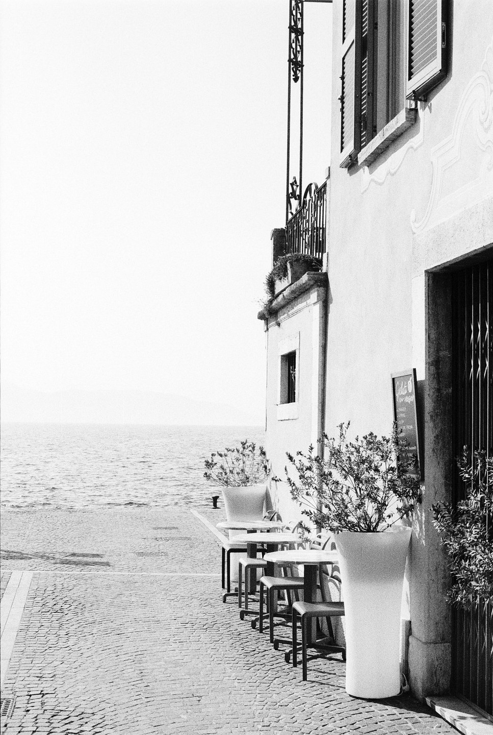 A cafe with outdoor seating is next to a body of water with mountains in the distance.