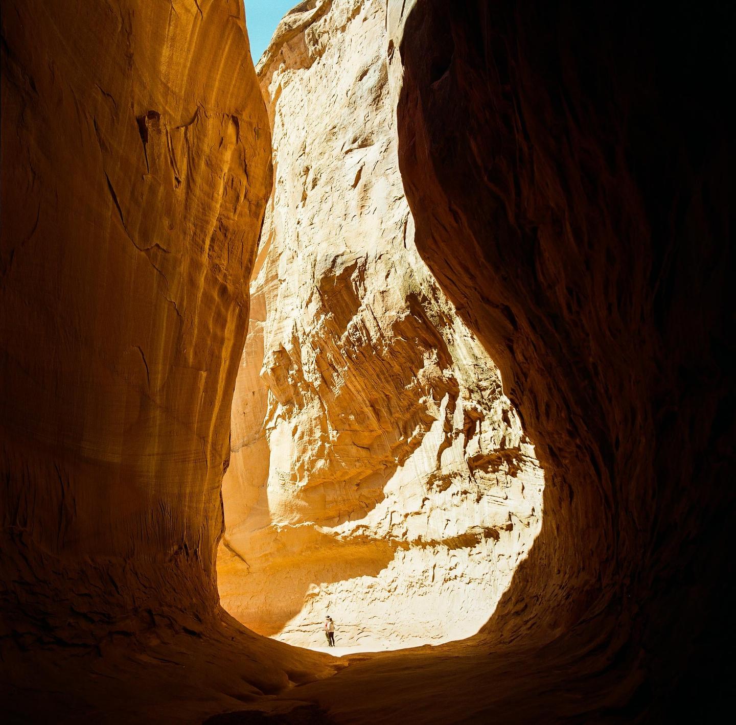 A person stands in a sunlit slot canyon with high rock walls.