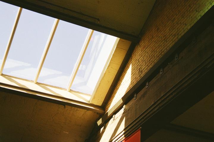 Sunlight streams through a skylight onto a textured ceiling and a brick wall.