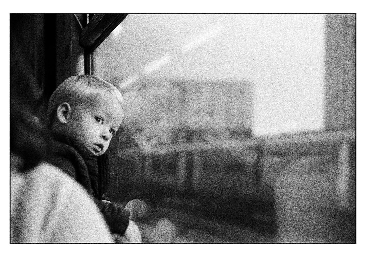 A child looks out a window with their reflection visible on the glass.
