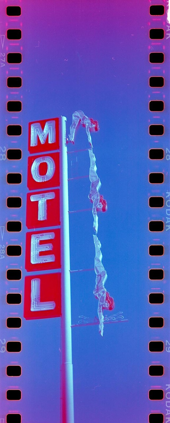 A neon motel sign is next to a pole with three acrobatic figures.