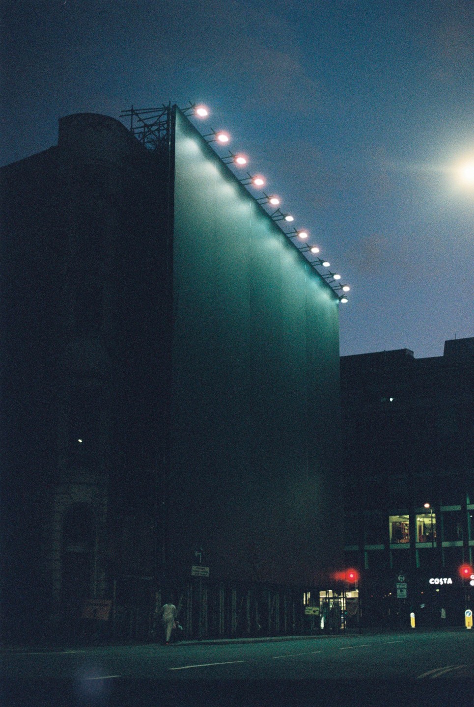 A large billboard with lights along its top edge stands next to a street at night.