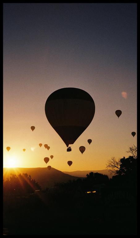 Hot air balloons float over a mountainous landscape at sunrise.